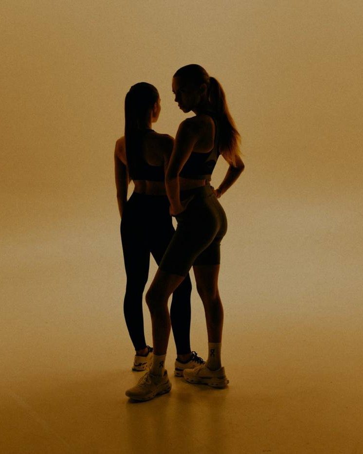 Two women training together, silhouetted against a warm orange backdrop